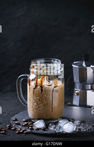 Mason Glas Eis Kaffee mit Eis und Schokolade Soße, serviert mit Kaffeebohnen und Eiswürfel auf Schiefer Steinplatte ov Stockfoto