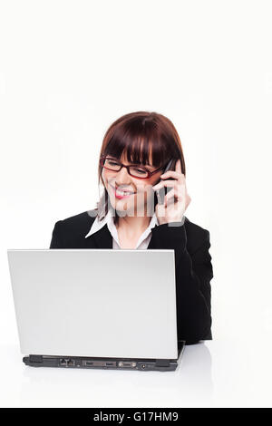 Geschäftsfrau blickte auf ihrem Laptop arbeiten und auch zu einer Unterhaltung auf ihrem Handy hören Stockfoto