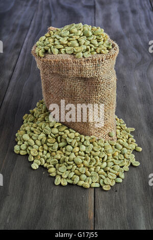 Grüne Kaffeebohnen in Leinensack auf alten Holztisch Stockfoto
