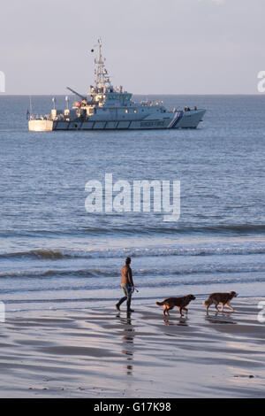 Eine Frau, die ihre Hunde Blick auf eine britische Grenze Force Schiff in Sandown Bay, Isle Of Wight Stockfoto