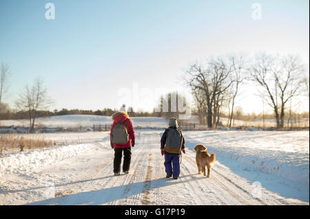 Golden Retriever und zwei junge Schwestern tragen Schulranzen gehen auf Schnee bedeckten Strecke, Ontario, Kanada Stockfoto