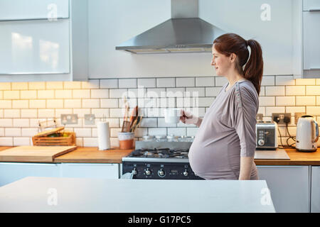 Schwangere Frau in der Küche halten Kaffeetasse Stockfoto