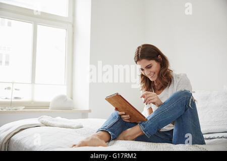 Schöne junge Frau sitzt auf Bett mit digital-Tablette Stockfoto