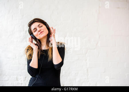 Schöne junge Frau wiegen, um Kopfhörer Musik vor weißer Wand Stockfoto