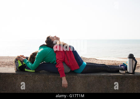 Läuferinnen, die einander in Brighton Beach an Wand gelehnt erschöpft Stockfoto