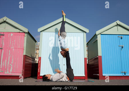 Mann und Frau üben akrobatische Yoga vor Strandhütten am Strand von Brighton Stockfoto