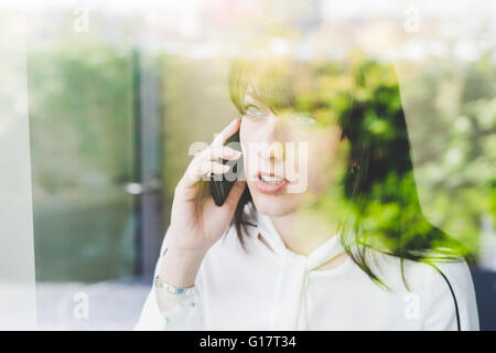 Fenster mit Blick auf junge Geschäftsfrau sprechen auf smartphone Stockfoto