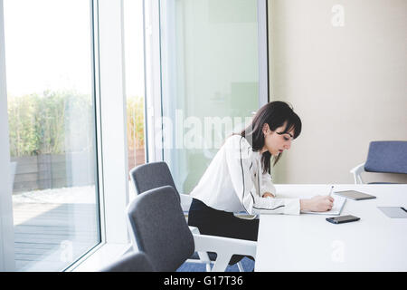 Junge Geschäftsfrau Schreiben von Notizen am Schreibtisch Stockfoto
