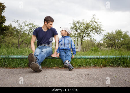 Glücklicher Vater und Sohn sitzen im Park. Lächelnd jungen Mann verbringt Zeit zusammen mit seinem Sohn Stockfoto