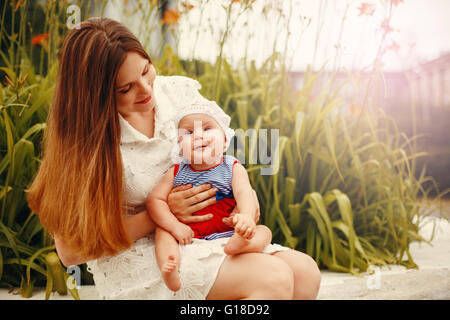 Niedliche glücklich Kleinkind auf liebevolle Mutter Knien sitzen und Lächeln auf den Lippen. Familienspaß. Bild mit warmen Farben abgeschwächt. Stockfoto