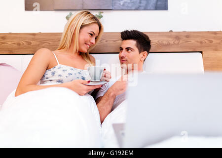 Paar zu Hause gemütlich im Bett mit Kaffee und Laptop zur hand Stockfoto