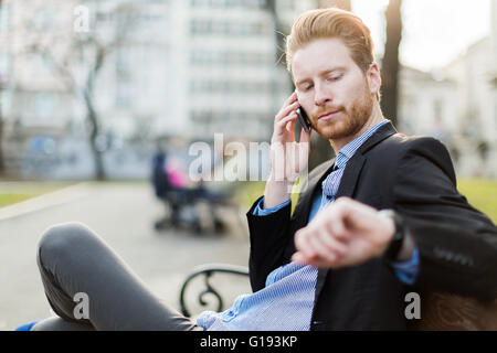 Blick auf seine Armbanduhr an einem sonnigen Tag in einem Stadtpark Geschäftsmann Stockfoto