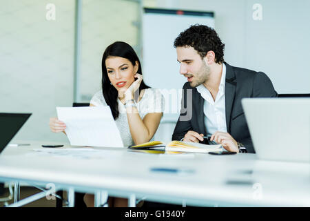 Junge, erfolgreiche Geschäftsfrau und ein Geschäftsmann, der Blick auf ein Papier beim Sitzen an einem Schreibtisch Stockfoto