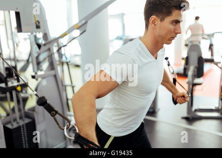 Gut aussehender Mann Ausbildung in klaren, modernen Fitnessraum auf verschiedenen Maschinen Stockfoto