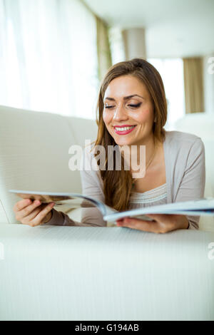 Schöne Frau auf einem Sofa ein Papier in einem gut beleuchteten stilvolle Wohnzimmer lesen Stockfoto