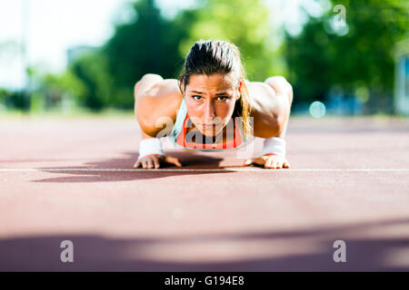 Junge schöne Frau doing Push-ups im Freien an einem heißen Sommertag konzentriert Stockfoto