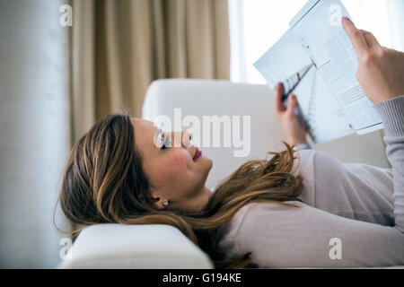 Schöne Frau auf einem Sofa ein Papier in einem gut beleuchteten stilvolle Wohnzimmer lesen Stockfoto