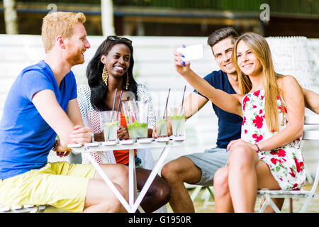 Eine Gruppe von Freunden einen Tisch sitzen und reden, Lächeln, während der Einnahme von Selfies an einem heißen Sommertag Stockfoto