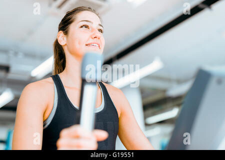 Schöne junge Dame mit dem elliptischen Trainer in einem Fitnessstudio in eine positive Stimmung Stockfoto