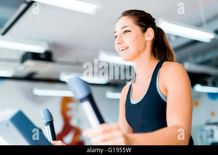 Schöne junge Dame mit dem elliptischen Trainer in einem Fitnessstudio in eine positive Stimmung Stockfoto