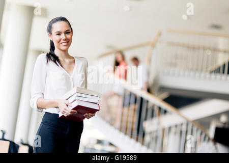 Schöne Frau halten Bücher und lächelnd in einer modernen Bibliothek Stockfoto