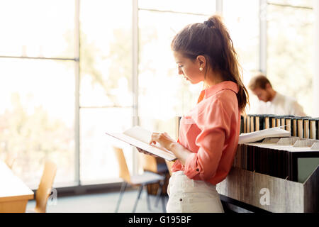 Schöne Frau, die ein Buch in einer Bibliothek und denken Stockfoto