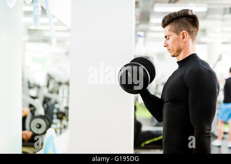 Hübscher Jüngling, trainieren Sie im Fitnessraum und Gewichte heben Stockfoto