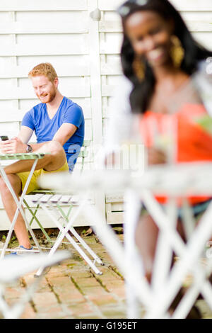 Gut aussehend glücklicher Mann hält Telefon in einem Café sitzen an einem Tisch im freien Stockfoto