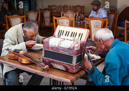 Zwei ältere Straßenmusikanten trinken Suppe in einem Restaurant mit einem Klavier, Akkordeon und Geige auf dem Tisch in Nessebar, Bulgarien Stockfoto