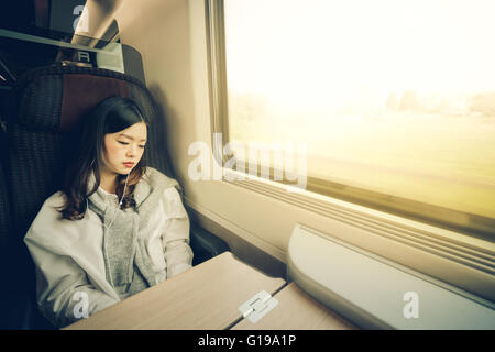 Schöne asiatische Mädchen schlafen im Zug beim Musikhören, mit Textfreiraum, weiches Licht Warmton Stockfoto