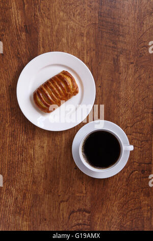 Schwarzer Kaffee in eine weiße Tasse und Gebäck auf weißen Teller overhead auf Holz senkrecht Stockfoto