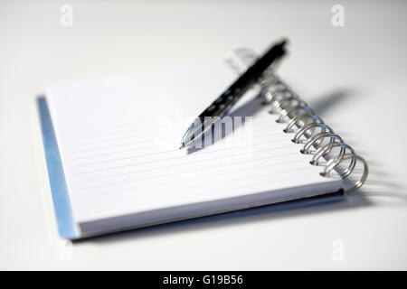 Notizblock mit Spiralbindung und schwarzem Stift, der oben auf einer weißen Oberfläche aufliegt – ein Konzept für Schreiben, Planen oder Notizen. Stockfoto