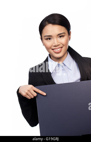 Stilvolle professionelle asiatische Dame zeigt mit dem Finger auf eine leere graue Zeichen, die sie in ihrer Hand hält lächelnd Stockfoto