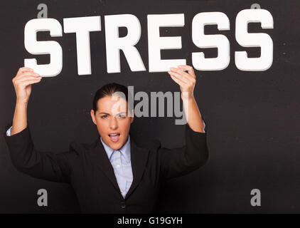 Betonte wütend attraktive Geschäftsfrau hält das Wort STRESS im weißen Schriftzug hoch über ihren Kopf auf einem schwarzen studio Stockfoto