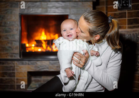 Mama Baby küssen, vor dem Kamin zu Hause Stockfoto