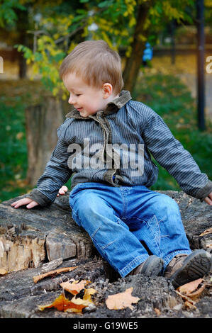 Junge sitzt auf einem Baumstumpf im Herbst Stockfoto