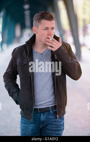 blonder Mann in Jeans zu Fuß die Straße und raucht eine Zigarette Stockfoto
