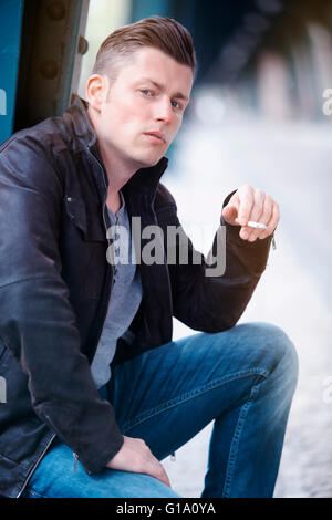 blonder Mann in Lederjacke, eine Zigarette rauchend Stockfoto