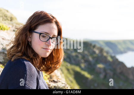 Junge Frau mit roten Haaren am Portmehor Point, Carn Galver, Cornwall, UK Stockfoto