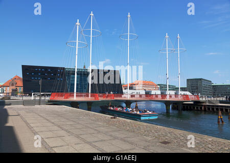 Eine Kanal-Kreuzfahrt-Schiff verläuft von Christianshavn Canal in Kopenhagen unter Cirkelbroen. Der schwarze Diamant ist im Hintergrund Stockfoto