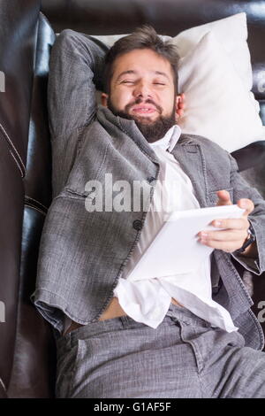 Verschlafene Geschäftsmann mit einem Tablet-Gerät auf einem sofa Stockfoto