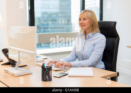 Middle aged business woman working at office on computer. Buildings Background Stockfoto