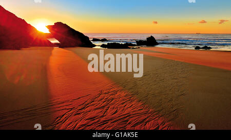 Portugal, Alentejo: Letzte Sonnenlicht Eingabe zwischen zwei Felsen leuchtenden nassen Sand am Strand bei Ebbe Stockfoto