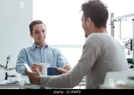 -Studenten mit einer Kaffeepause am Schreibtisch, halten sie Tassen, 3D-Drucker im Hintergrund Stockfoto