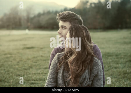 Junge Teenager im Freien, auf dem Rasen sitzen und kuscheln, umarmt er seine Freundin, Beziehungen und Gefühle Konzept Stockfoto