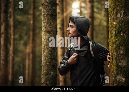 Junger hübscher Mann zu Fuß in einem Wald und schaut sich um, Natur und Exploration Konzept