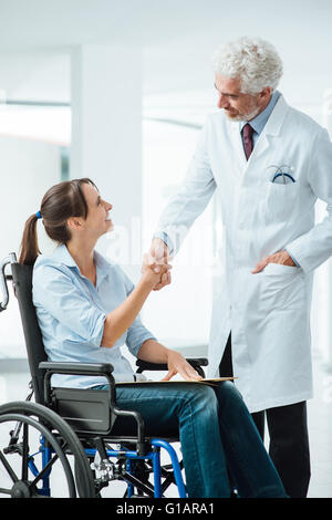 Sie ist zuversichtlich Lächeln Arzt Händeschütteln mit seinem neuen Patienten, eine junge Frau im Rollstuhl Stockfoto