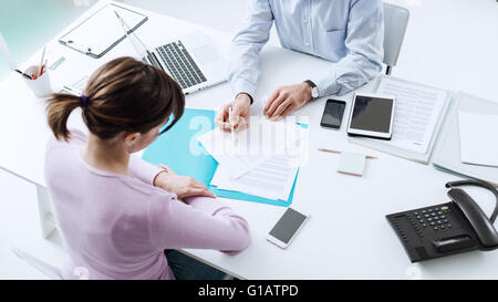 Berater treffen mit einem Kunden in sein Büro, er erklärt ein Vertragsdokument und Politik, die Frau sitzt an seinem Schreibtisch Stockfoto