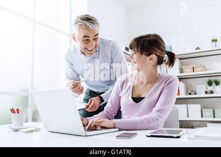 Fröhliche Geschäftsleute im Büro, sie arbeiten zusammen und Lächeln, die Frau ist die Eingabe auf einem laptop Stockfoto
