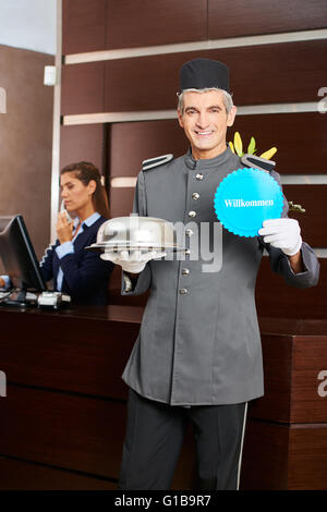 Hotelseite halten deutsche Schild mit der Aufschrift "Willkommen" (willkommen) an der Rezeption Stockfoto